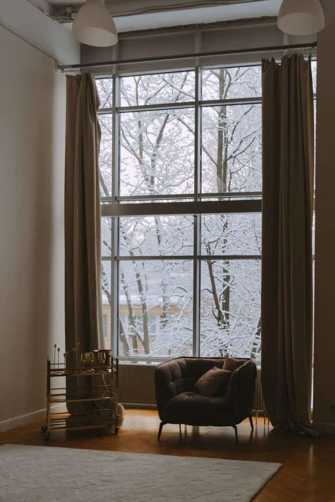 Armchair beside large windows with snow outside, the chilly seat near the glass that insulating film is meant to fix