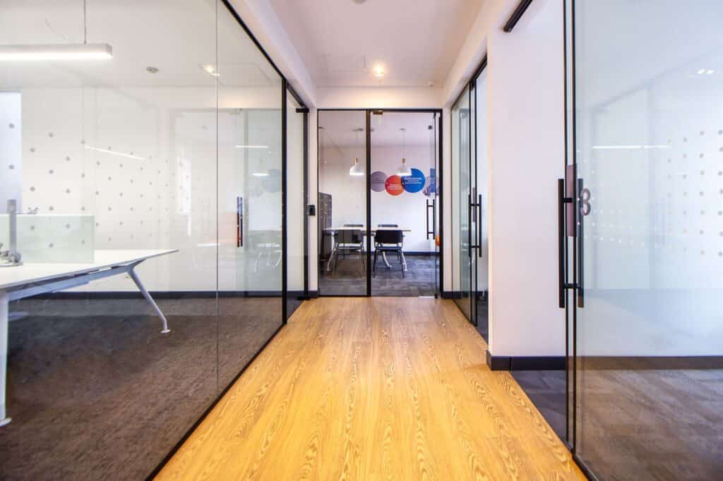 Bright office hallway lined with glass walls, where smart film can switch meeting rooms from clear to private